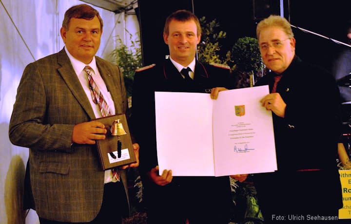 Urkunde und eine provisorische Goldene Glocke: v.l. Innen-Staatssekretär Volker Dornquast, Heides Wehrführer Robert Rosin sowie der Entdecker Bernhard von Oberg.